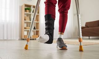 Man walking with crutches wearing an ankle support brace during recovery from ankle surgery