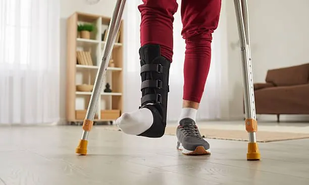 Man walking with crutches wearing an ankle support brace during recovery from ankle surgery