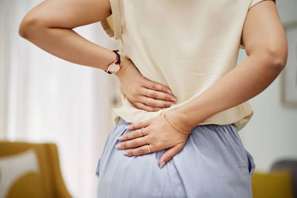 Woman with back discomfort at home, illustrating symptoms of spinal stenosis treated with physiotherapy