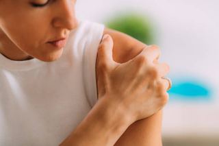 Woman holding her shoulder in pain, illustrating the stiffness and reduced movement of frozen shoulder treated with physiotherapy