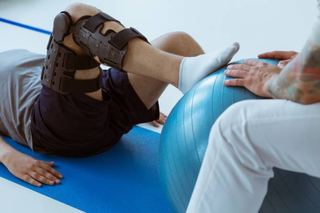 Patient sitting on a gym mat training with an exercise ball during post-operative rehabilitation at home